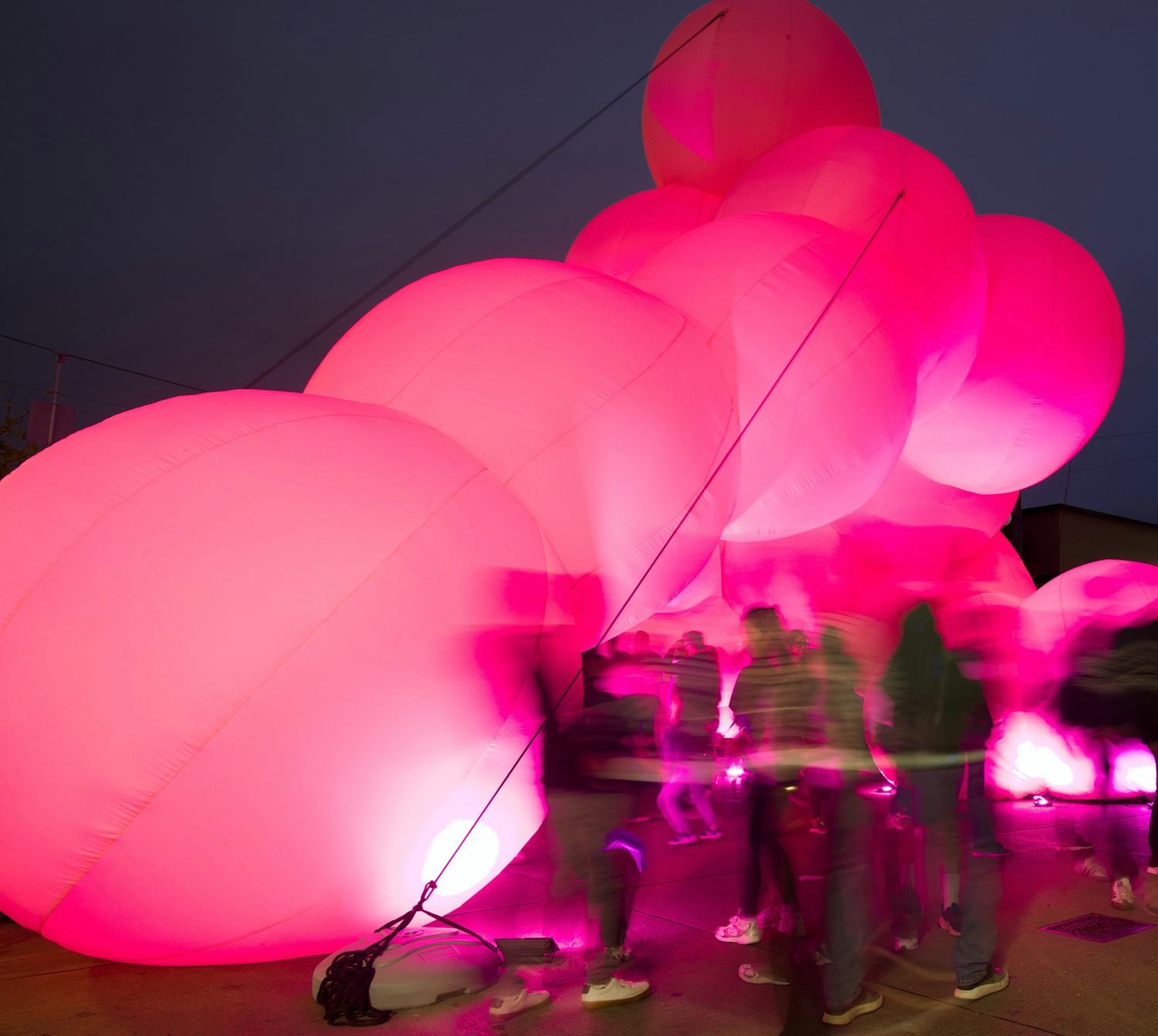 Estructura inflable rosada y luminosa de noche, con gente a sus pies