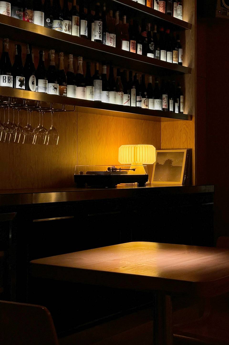 Barra de un bar de vinos con una lámpara encendida y estantes de botellas en penumbra