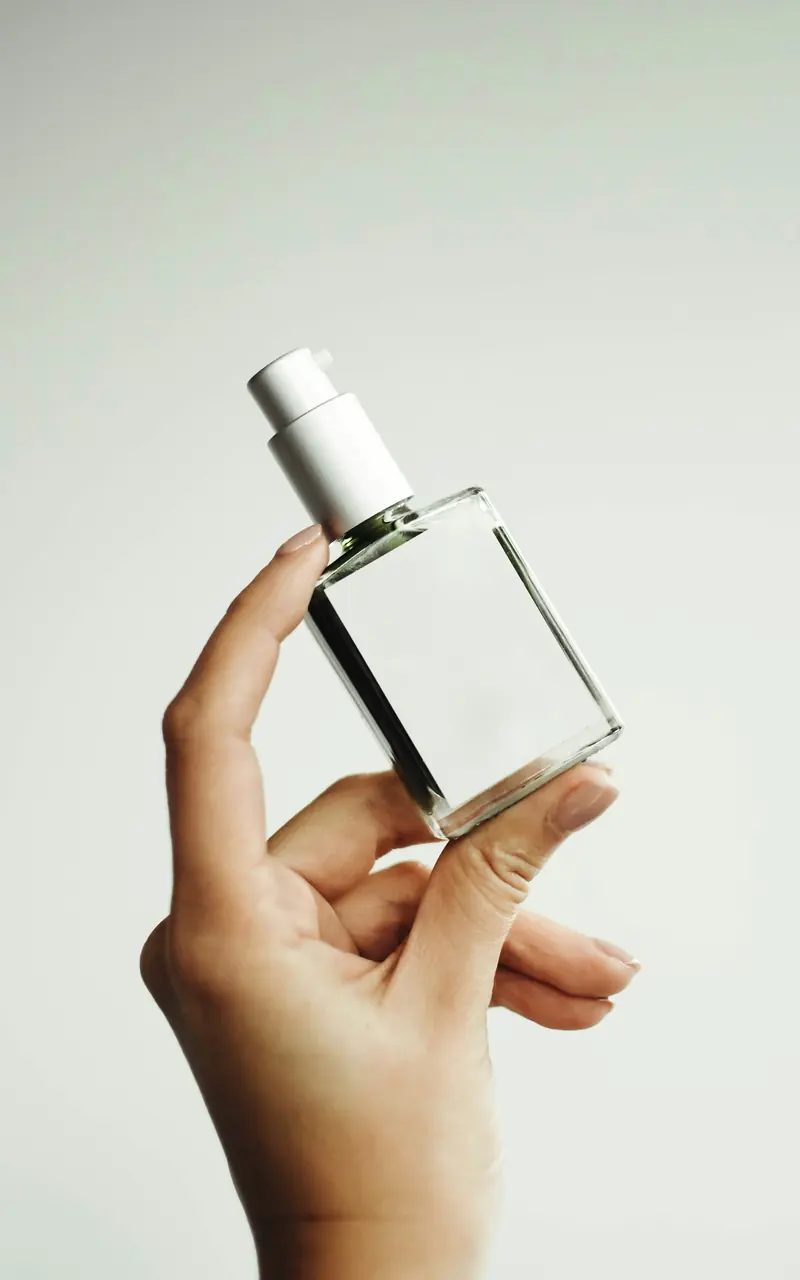 Mano sosteniendo un frasco de perfume transparente sobre fondo claro