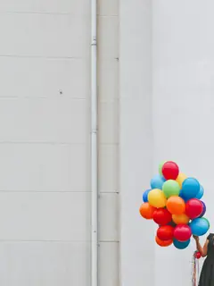 Persona de espaldas con un racimo de globos frente a un muro blanco