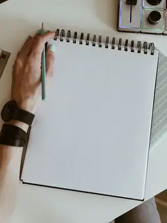 Mano sobre una libreta en blanco junto a lápices