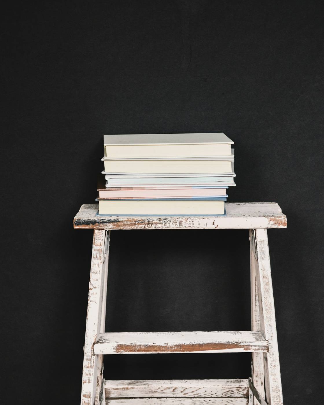 Pila de libros sobre un taburete blanco, con fondo negro