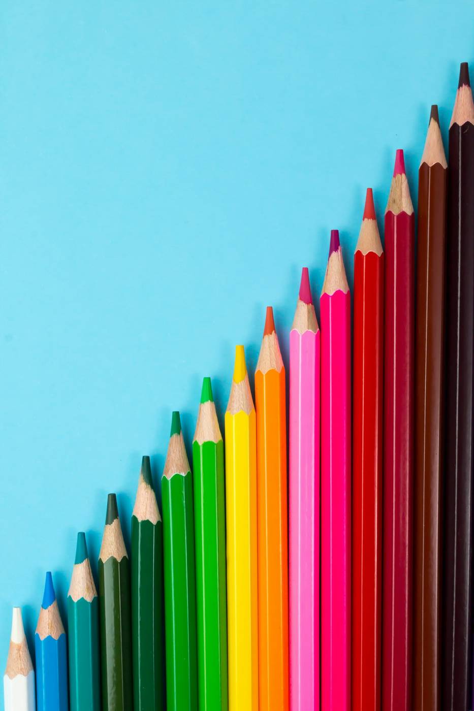 Lápices de colores ordenados en diagonal sobre un fondo celeste