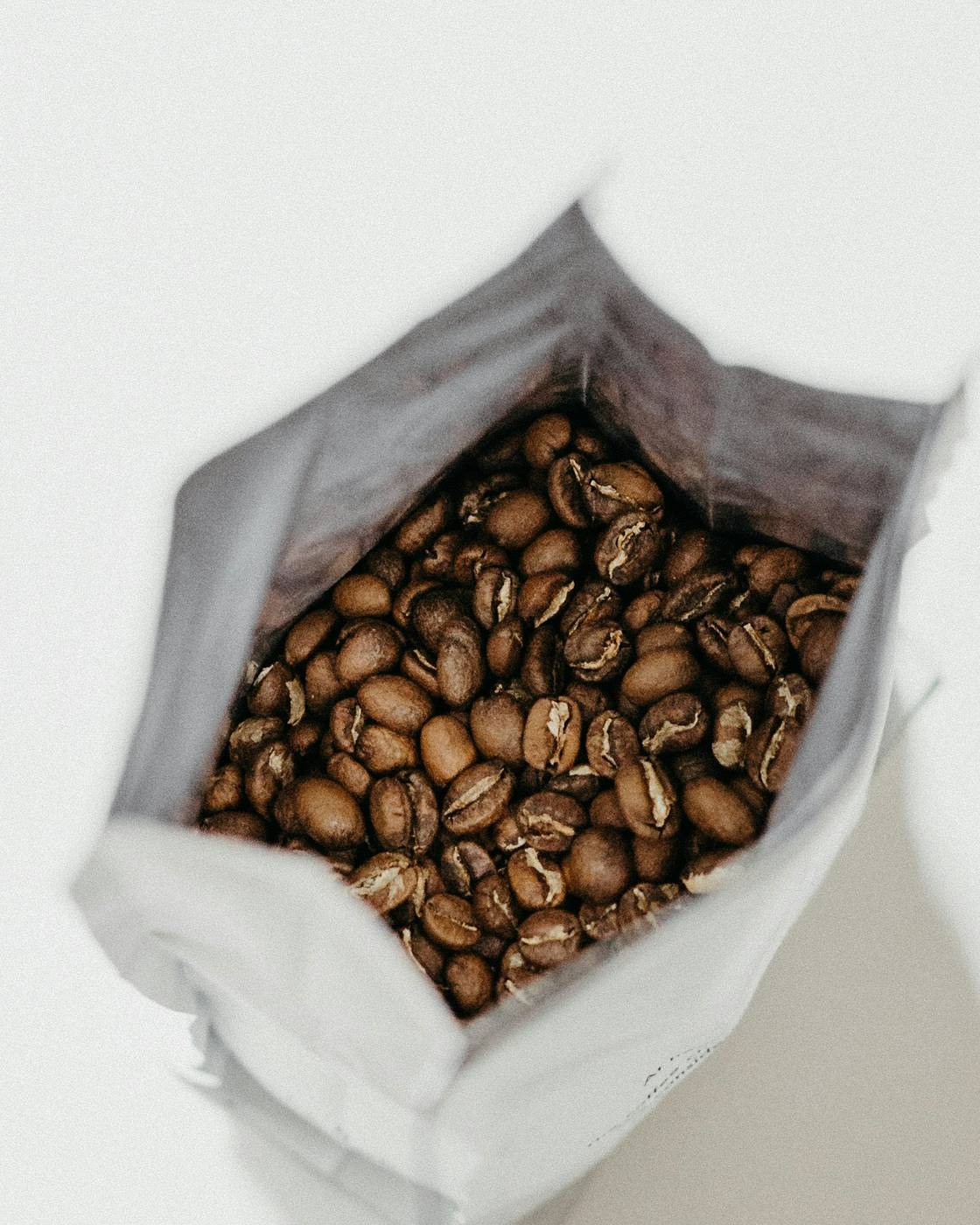 Granos de café tostado dentro de una bolsa abierta de papel blanco