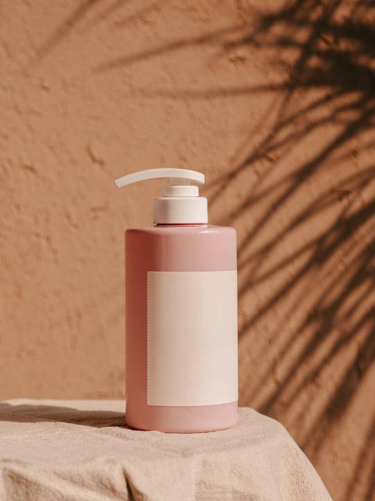 Envase rosado sin rótulo sobre un paño, con la sombra de una palma en la pared