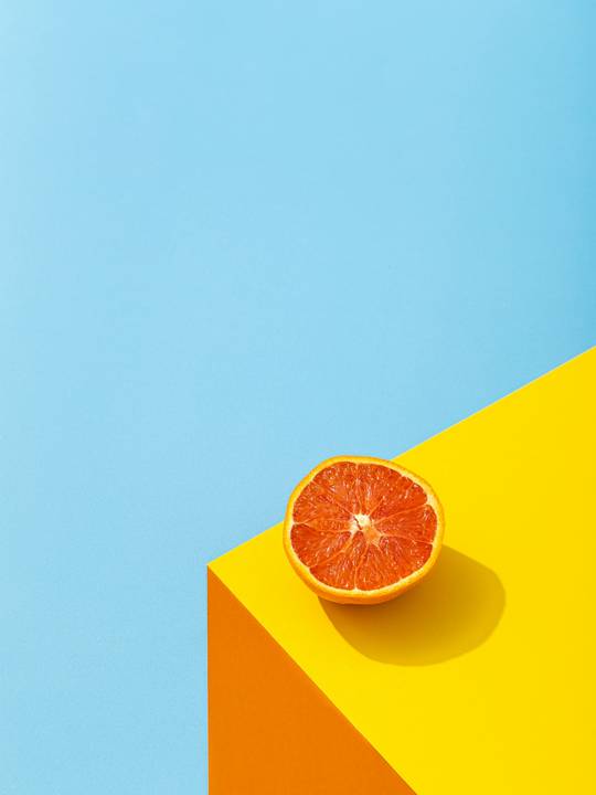 Media naranja sanguina sobre un cubo amarillo y celeste