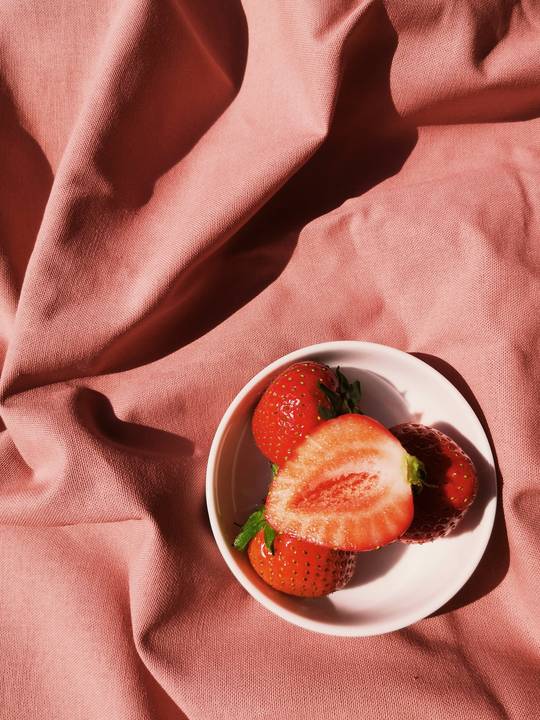 Fresas partidas en un cuenco blanco sobre una tela rosa polvo