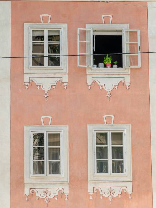 Fachada rosada con ventanas blancas y una de ellas abierta