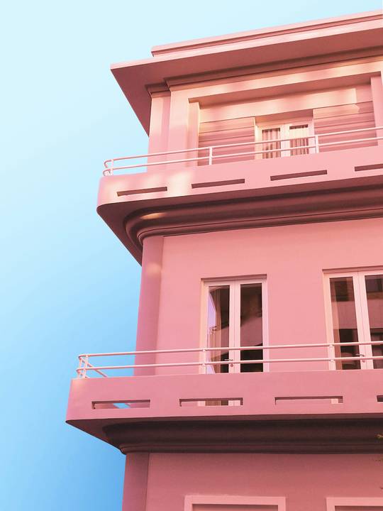 Fachada rosada con balcones, vista desde abajo contra el cielo