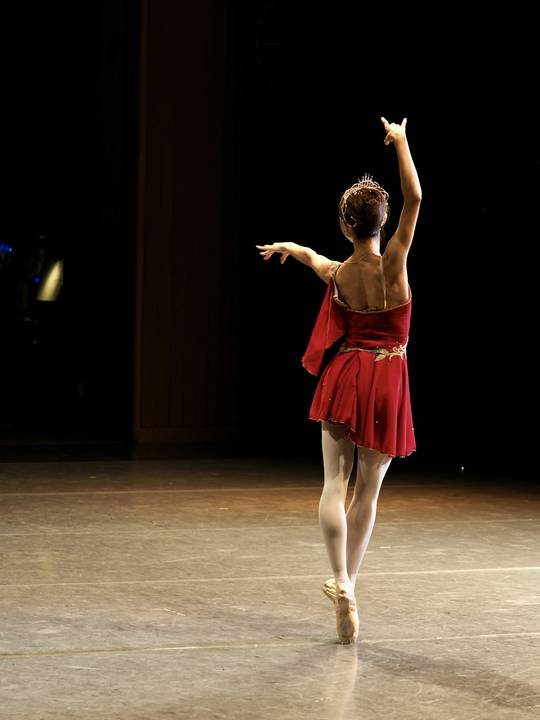 Bailarina de espaldas con vestido rojo sobre un escenario oscuro