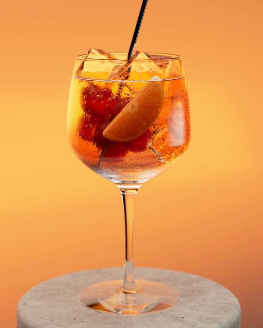 Copa con fruta y una pajilla sobre un pedestal de cemento, fondo naranja