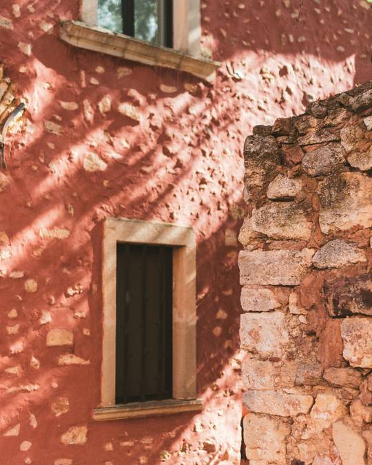 Muro color terracota con una ventana y sombras de hojas