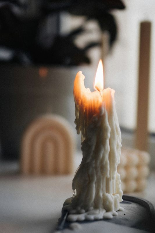 Vela blanca de cera escurrida con la llama encendida, frente a otras velas desenfocadas