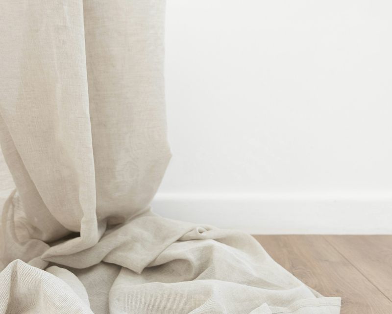 Cortina de lino claro que cae al suelo de madera, junto a una pared blanca