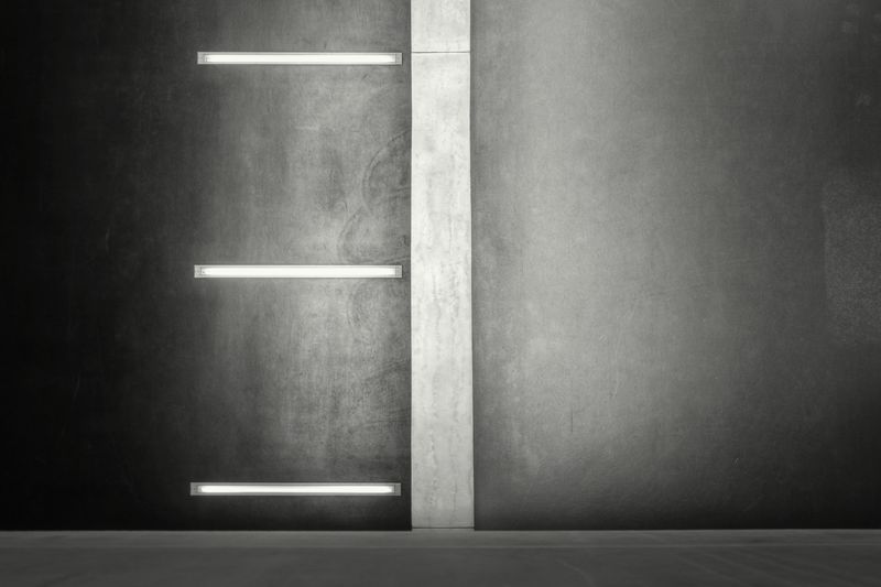 Tres tubos de luz empotrados en un muro oscuro junto a una franja de hormigón claro