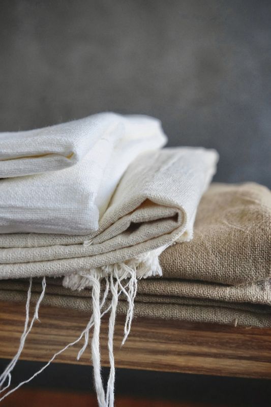 Primer plano de paños de lino blanco y beige apilados con flecos sueltos