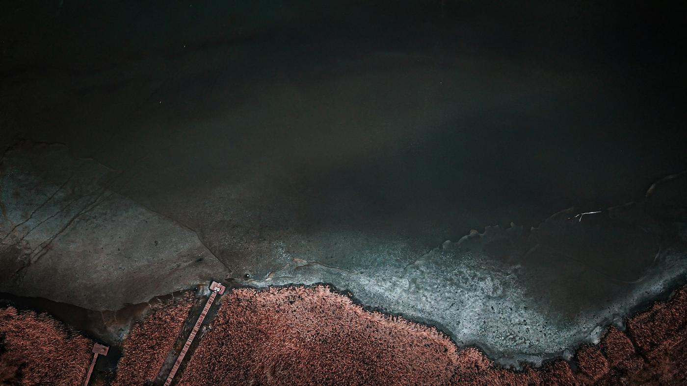 Orilla oscura de agua con costra de sal y tierra rojiza, vista aérea