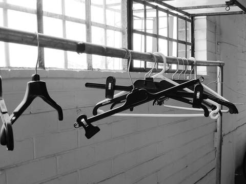Perchas colgadas de una barra frente a una ventana, en blanco y negro