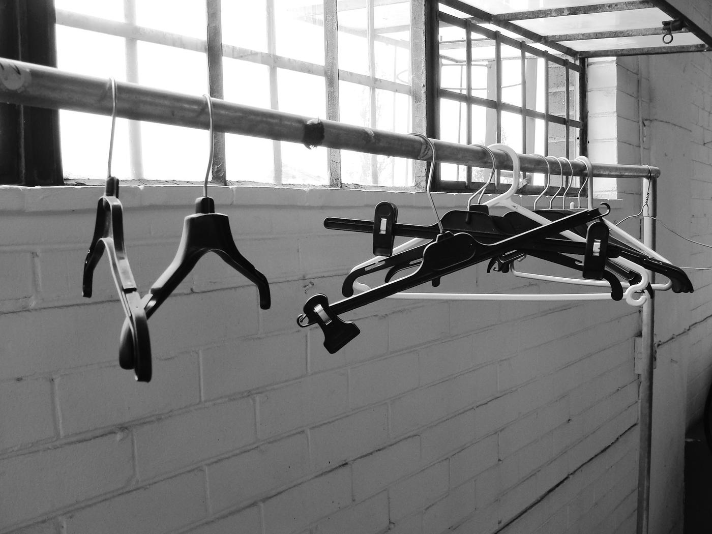 Perchas colgadas de una barra frente a una ventana, en blanco y negro