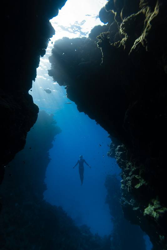 Figura diminuta bajo una grieta de luz en una cueva submarina