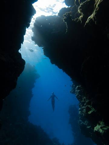 Figura diminuta bajo una grieta de luz en una cueva submarina