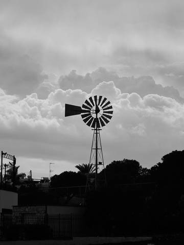 Silueta de un molino de viento contra un cielo cargado, en blanco y negro