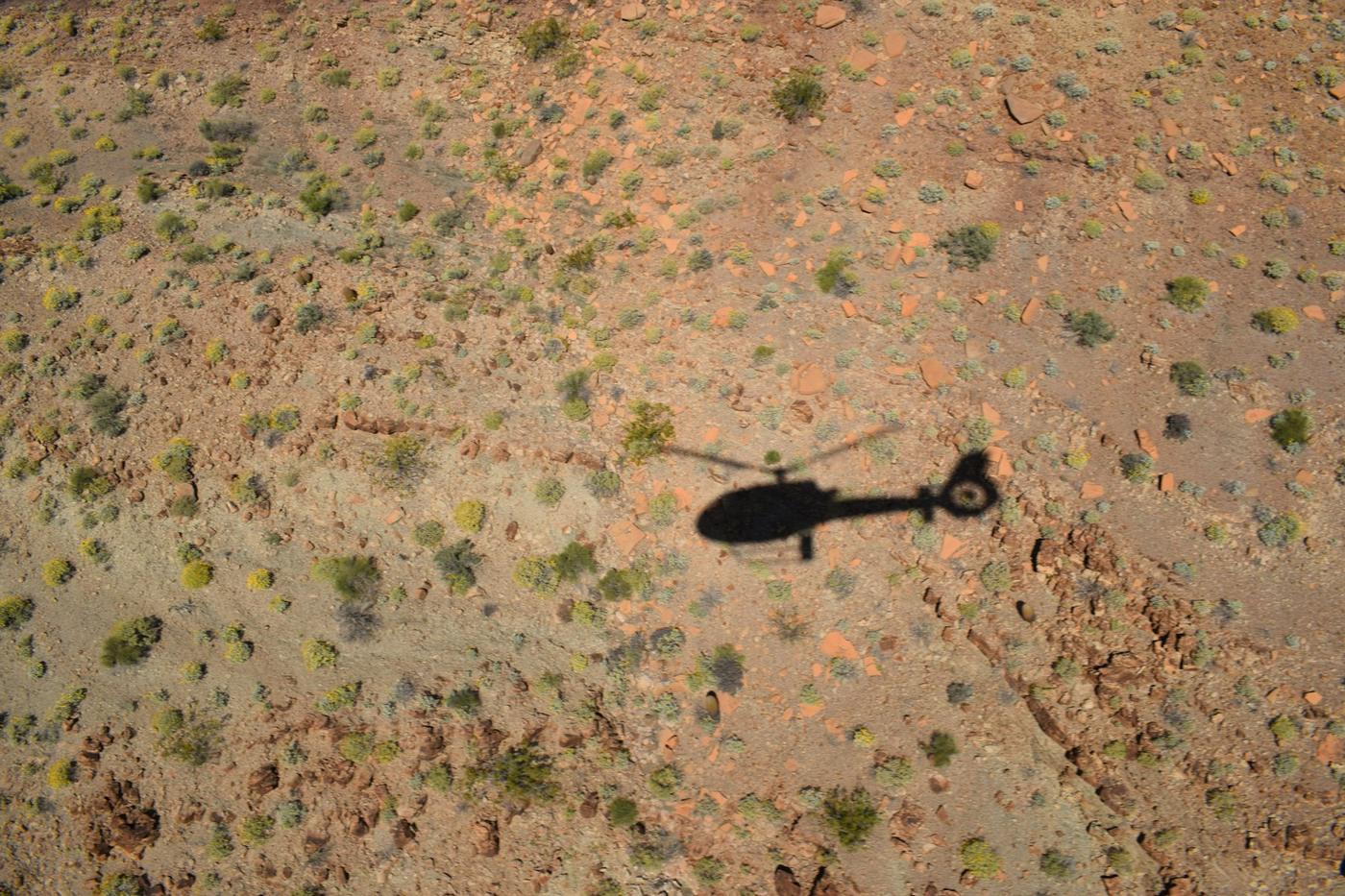 Sombra de un helicóptero sobre tierra roja con matorrales