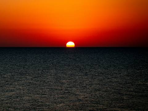 Sol rojo sobre el horizonte y un mar oscuro