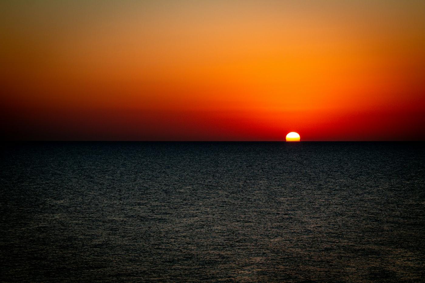 Sol rojo sobre el horizonte y un mar oscuro