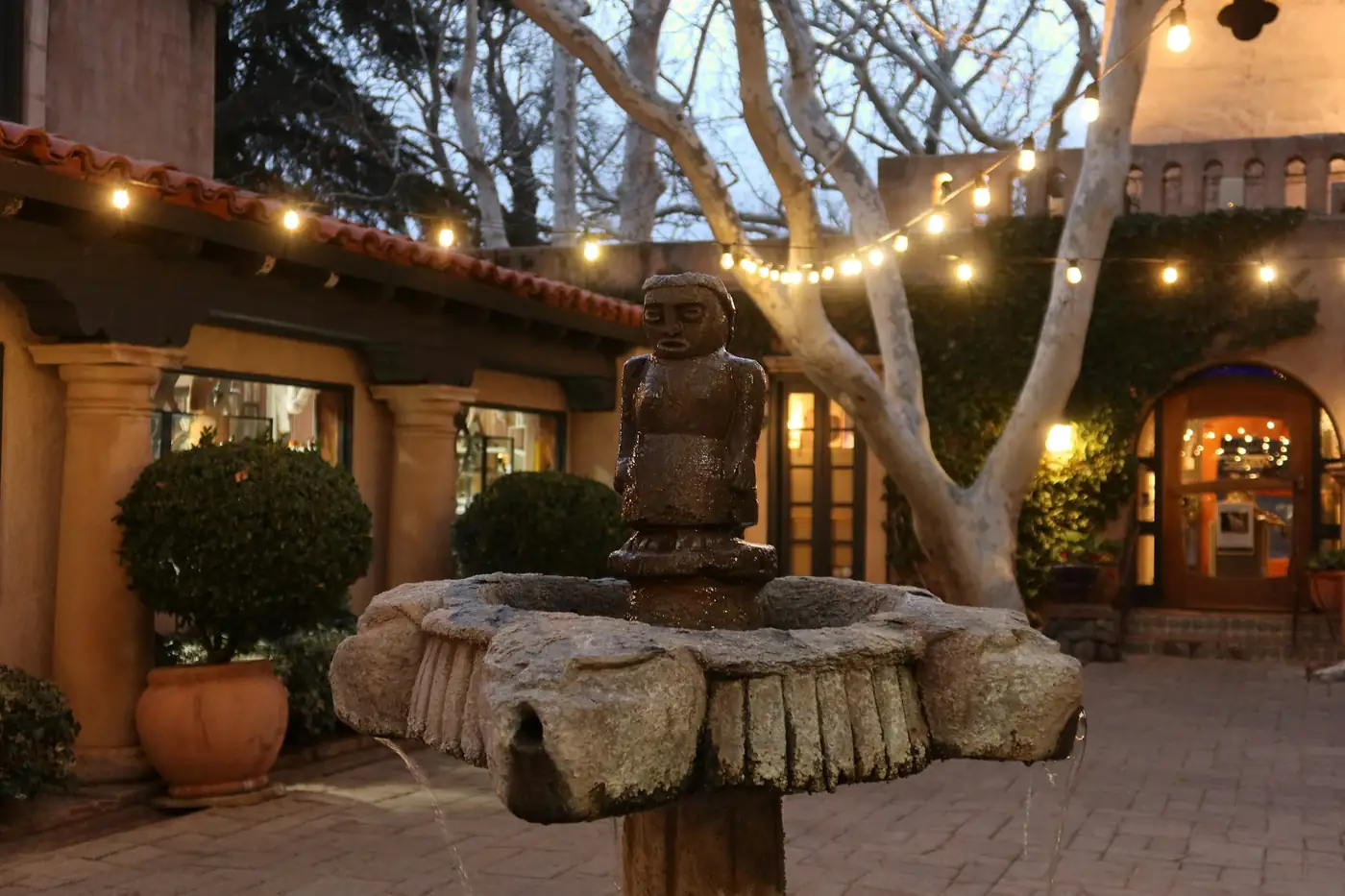 Patio con guirnaldas de luz y una fuente al anochecer