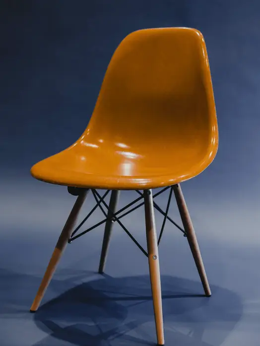 Silla de concha naranja con patas de madera sobre un fondo azul