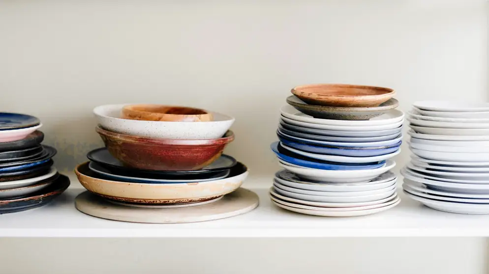 Pilas de platos y cuencos de colores sobre un estante blanco
