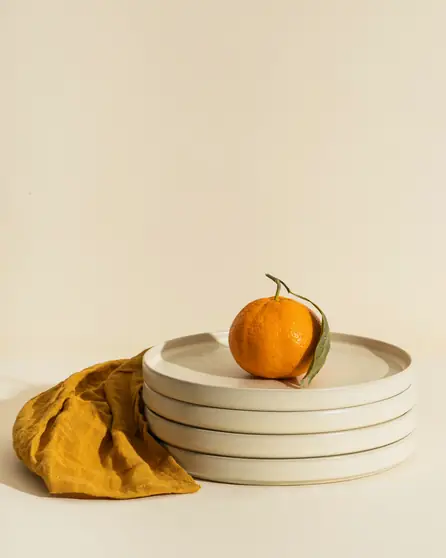 Platos apilados con una naranja sobre una tela mostaza