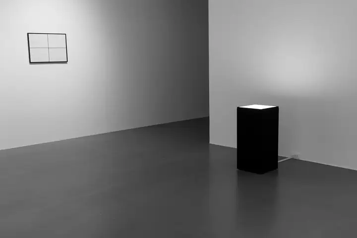 Peana negra en una sala gris, junto a un cuadro en la pared