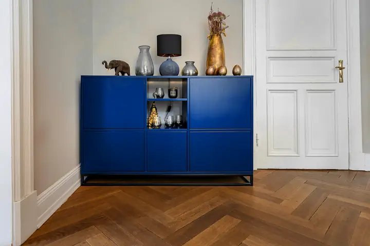Mueble bajo turquesa con objetos encima, sobre un piso de espiga