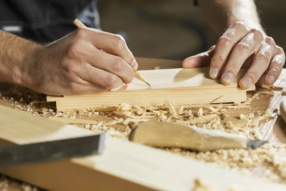 Manos marcando una pieza de madera entre virutas