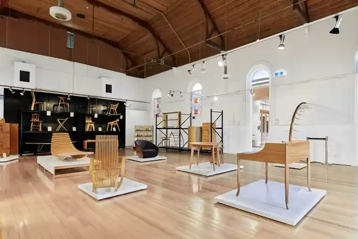 Sala de exposición con sillas y mesas de madera sobre tarimas blancas