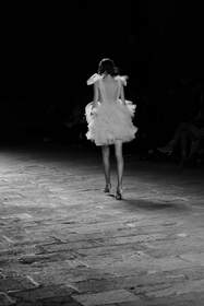 Figura de espaldas con falda de volantes en una pasarela, en blanco y negro