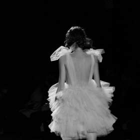 Figura de espaldas con falda de volantes en una pasarela, en blanco y negro
