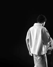 Figura de espaldas con chaqueta crema sobre un escenario oscuro