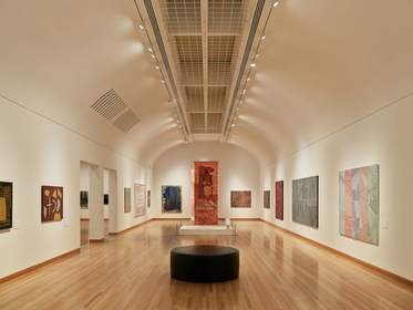 Sala larga de un museo con suelo de madera y obras en las paredes