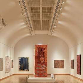 Sala larga de un museo con suelo de madera y obras en las paredes