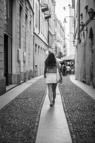 Figura de espaldas que camina por un callejón empedrado, en blanco y negro