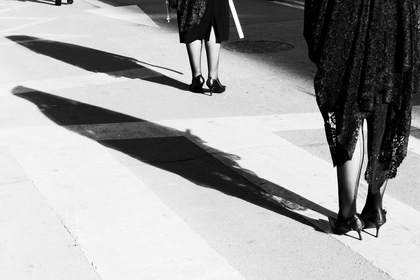 Piernas y una sombra larga sobre un paso peatonal, en blanco y negro