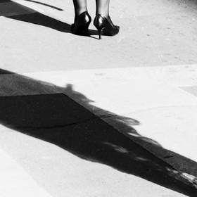 Piernas y una sombra larga sobre un paso peatonal, en blanco y negro