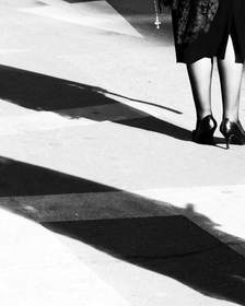 Piernas y una sombra larga sobre un paso peatonal, en blanco y negro