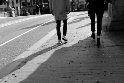 Dos figuras que caminan con sombras largas por una calle de adoquines