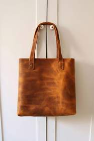 Bolso de cuero caramelo colgado de una puerta blanca