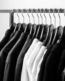 Camisas y chaquetas colgadas de una barra delante de una pared blanca