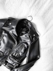 Chaqueta de cuero negro con cierre diagonal sobre una tela blanca